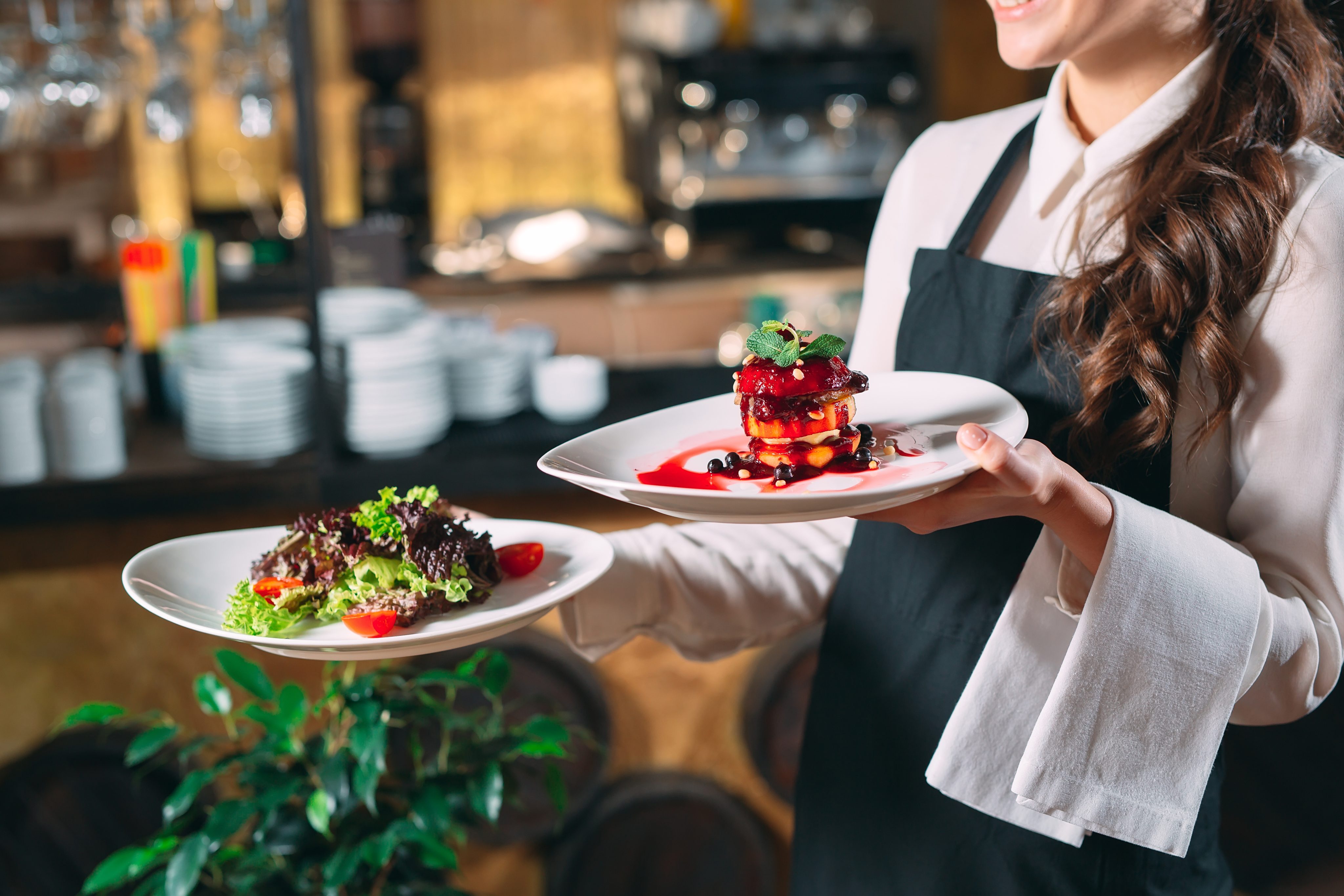 A waitress holding a plate of locally-sourced gourmet salad and a dessert in a Huntington Beach, California restaurant.
